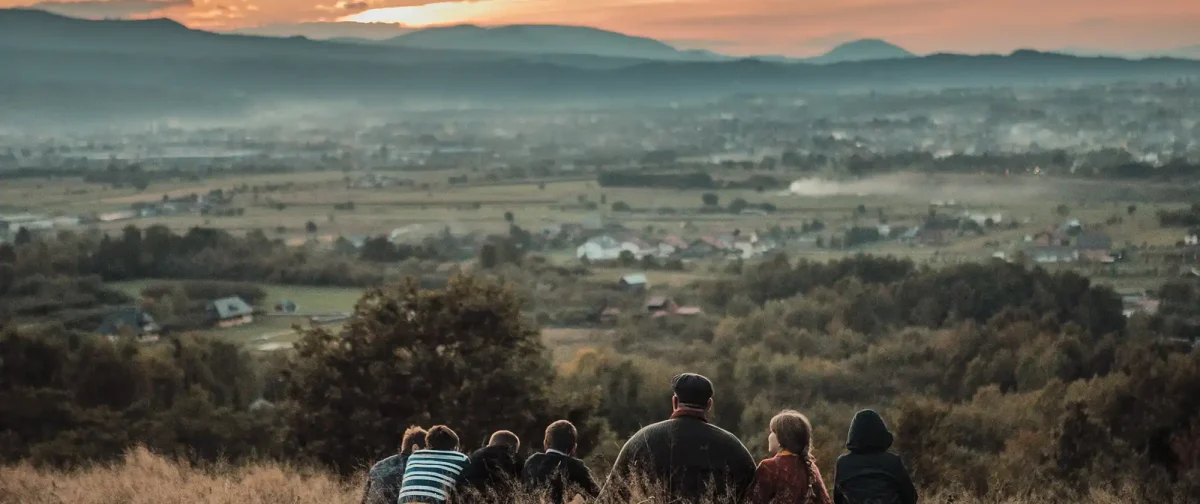 Man and children sitting in meadow at sunset, looking out over town in valley below